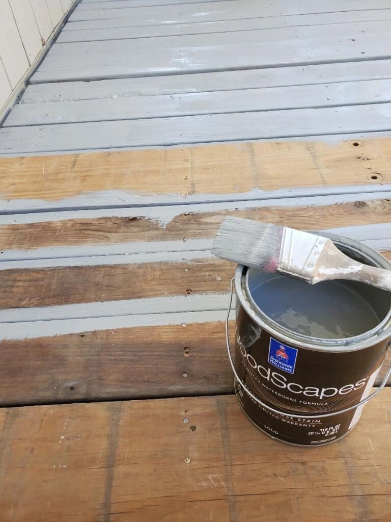 Open stain can and brush on a deck being coated grey